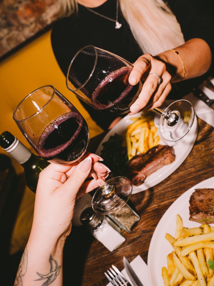 two people enjoying a steak dinner with bottle of house wine at revolution bars