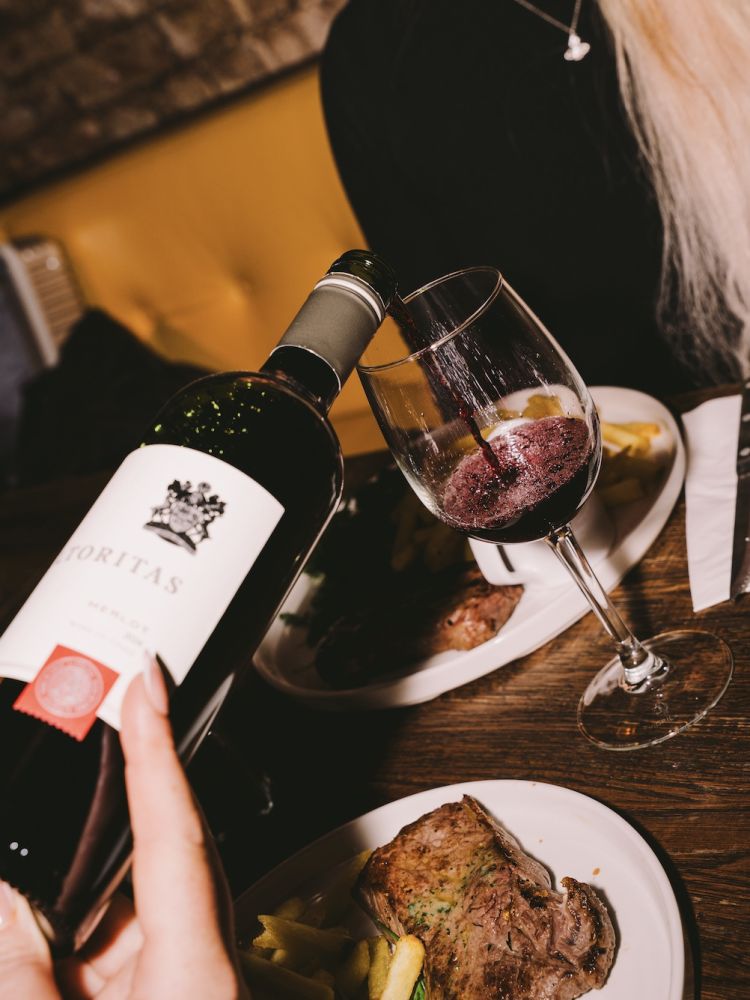 two people enjoying a steak dinner with bottle of house wine at revolution bars