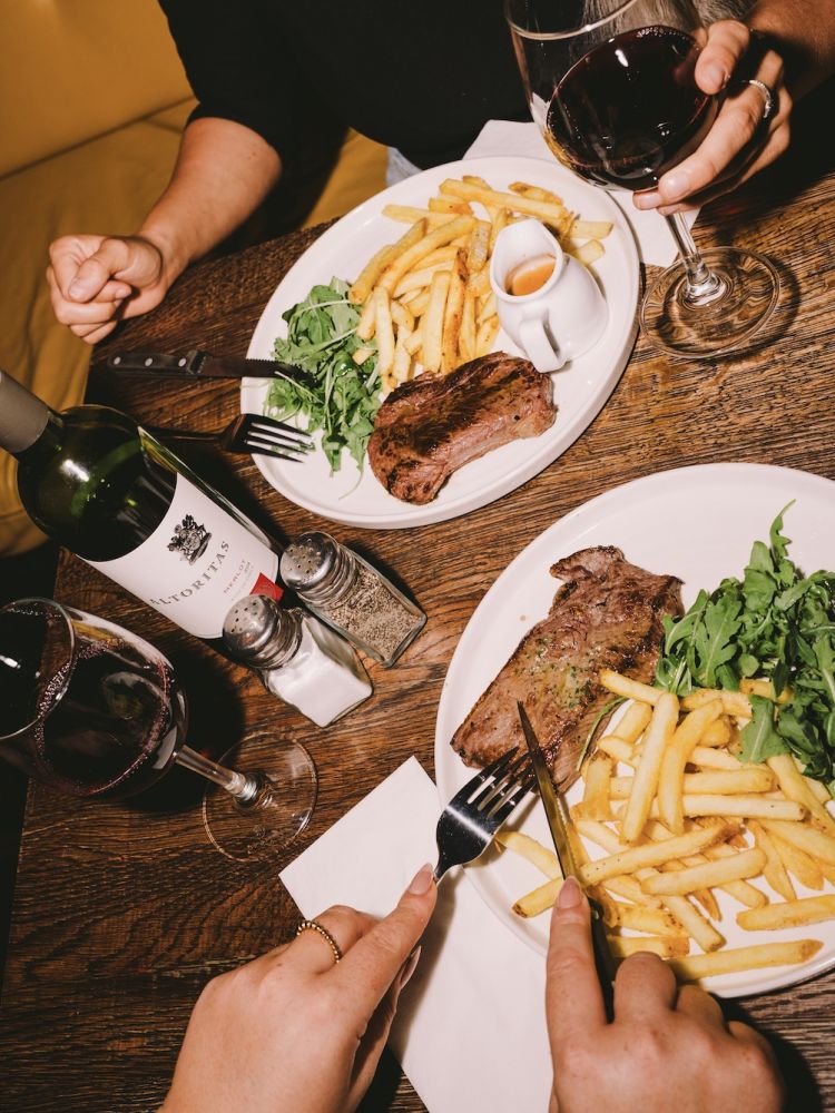 two people enjoying a steak dinner with bottle of house wine at revolution bars