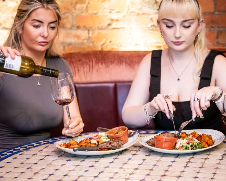two ladies enjoying a steak meal and bottle of house wine at revolución de cuba