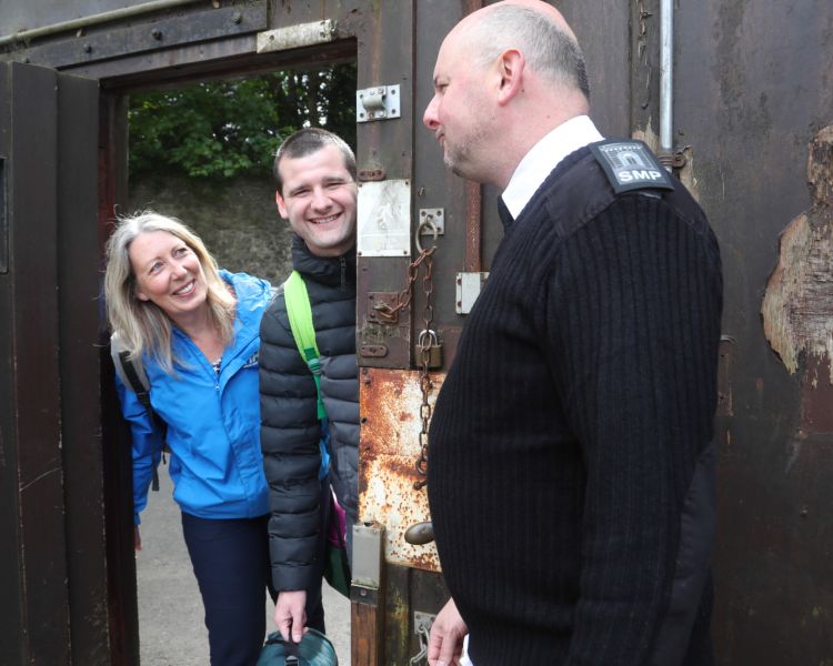 man and woman looking through the gate with prison officer looking on on a night behind bars experience