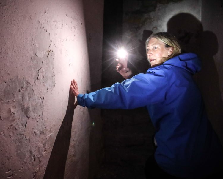 woman holding a torch in the dark as she climbs stairs on a night behind bars experience