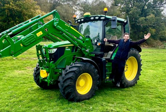 man posing for photo hanging on to the side of a tractor on a tractor driving experience