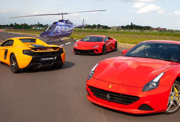 three supercars on a track with a helicopter in the background