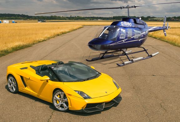 a yellow supercar on a track with a blue helicopter behind it