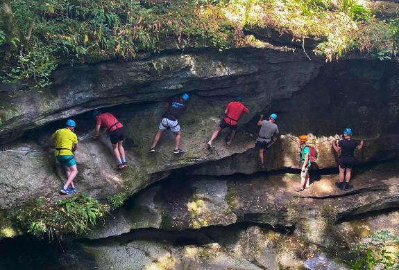 people walking and climbing along the edge of a gorge overlooking a river
