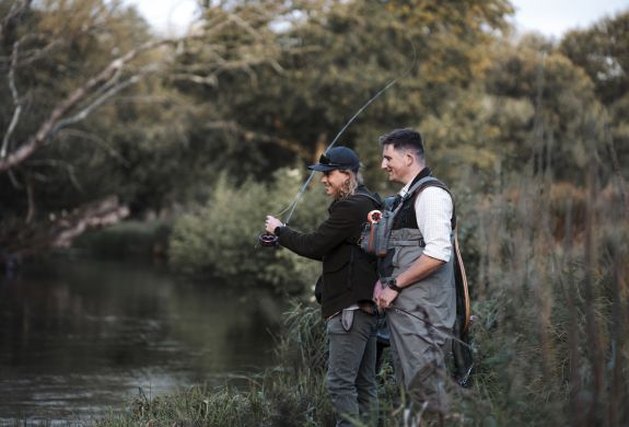 man learning to fly fish with guide by side of river