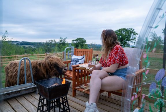 A lady and highland cow by a fire pit on the sunset pizzas experience