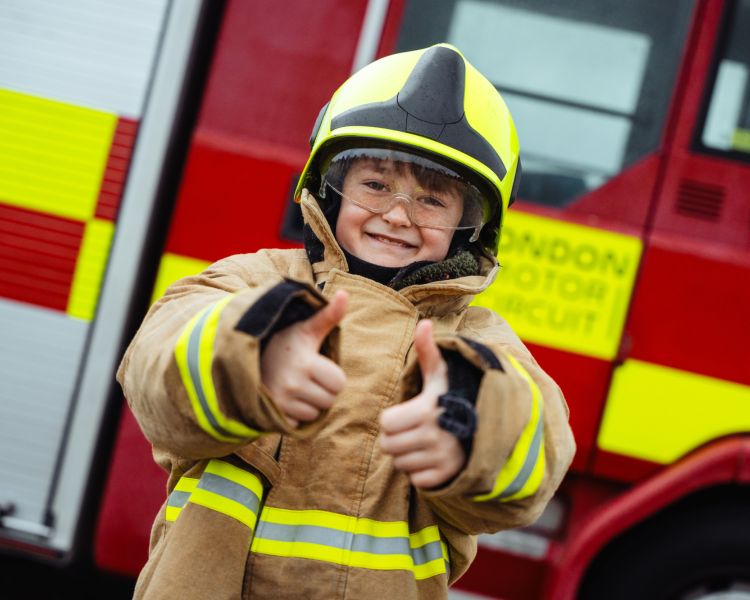 young boy dressed in firemans outfit in front of fire engine for family driving day