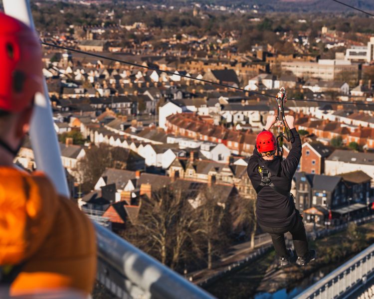 Man zip lining at zip world cardiff with houses in background