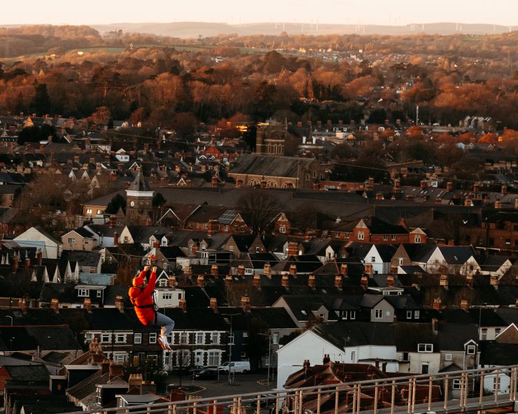Person zip lining at zip world cardiff with houses in background