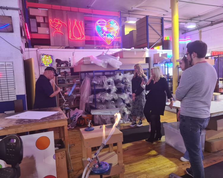 group watching craftsperson on neon sign taster session