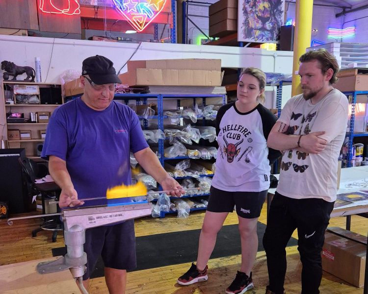 man having a go at bending glass watched by others on neon sign taster session
