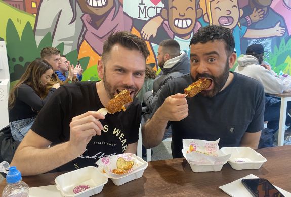 Two men eating corndogs on manchester food tour