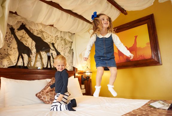 two young kids bouncing on bed in the giraffe room at the safari hotel at chessington world of adventures
