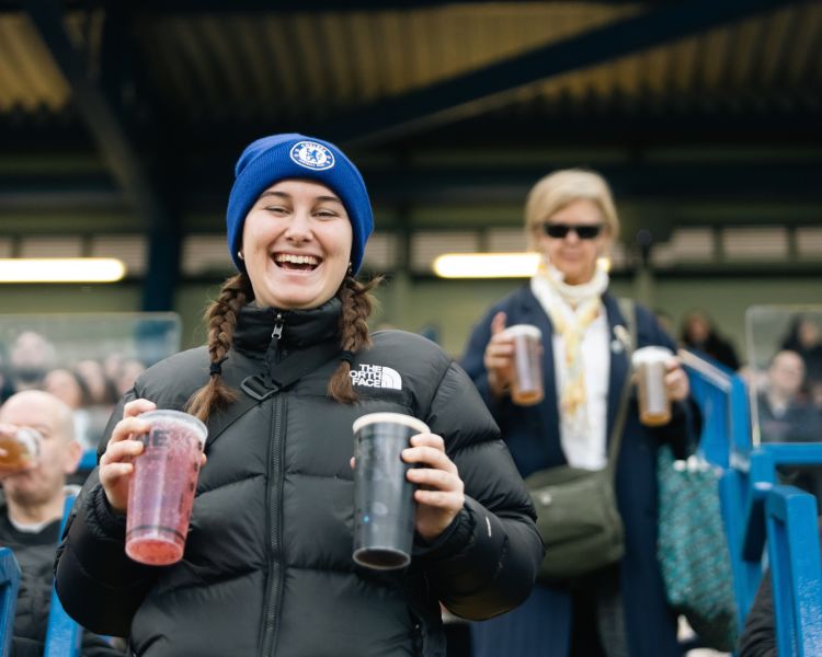 Women holding drinks walking to seats in stand at stamford bridge