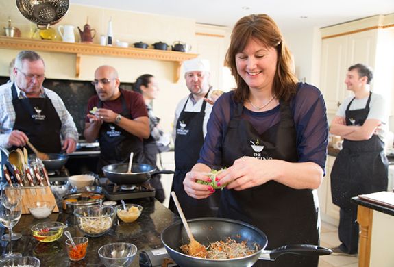 people being taught a cookery lesson in a kitchen with the help of professional chefs on a cookery course experience day