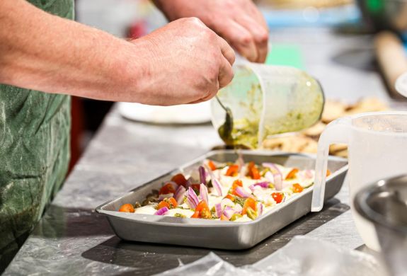 drizzling oil over focaccia ready to bake on continental bread making workshop