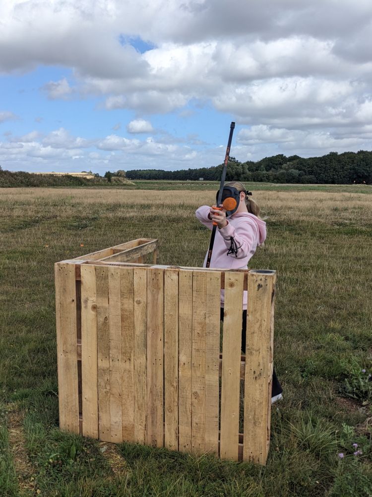 girl behind wooden boards shooting a combat archery arrow