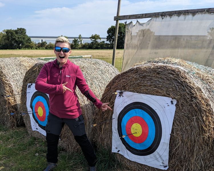 person posing next to archery target with an arrow in middle