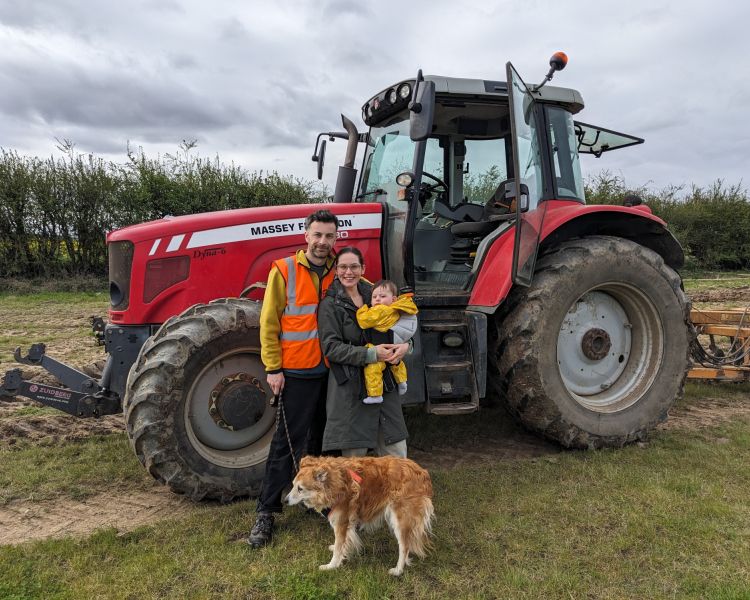 couple with baby and dog posing next to tractor on a tractor driving experience