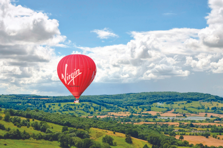 red virgin hot air balloon floating over countryside