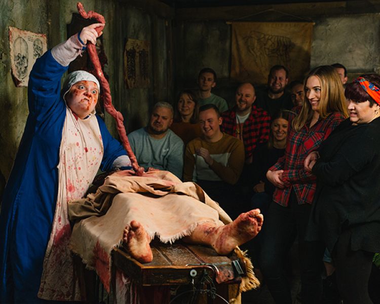 visitors watching a man pull out the insides of a dead body as part of the london dungeon experience in london