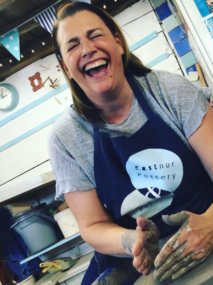 woman laughing while moulding clay on a potters wheel on a pottery experience day