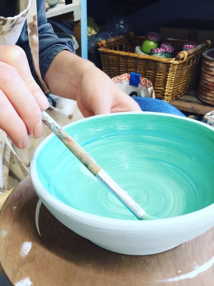 person painting green glaze onto a bowl on a pottery course experience day