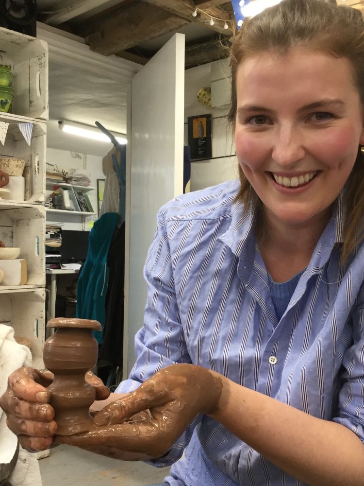 woman smiling while holding her clay creation made on a pottery course experience day