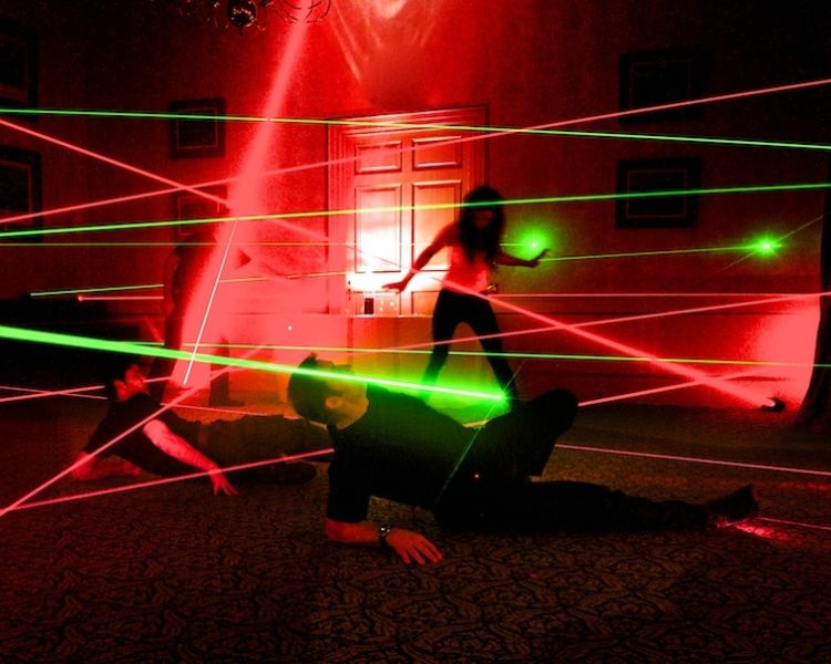 three people trying to make their way through a room lit up with laser beams on a spy camp experience day