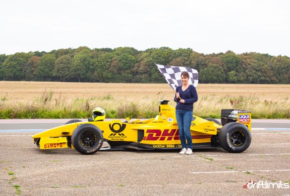 woman holding chequered flag next to f1 jordan car on a f1 car photoshoot and passenger lap experience