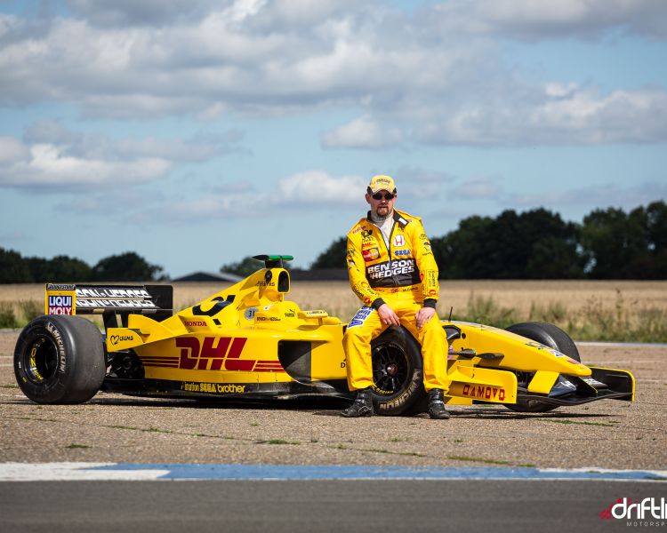 man in yellow driving suit sat on an f1 jordan car on a f1 car photoshoot and passenger lap experience