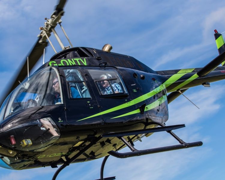 a black helicopter with green stripes in the air for a helicopter ride experience with adventure 001