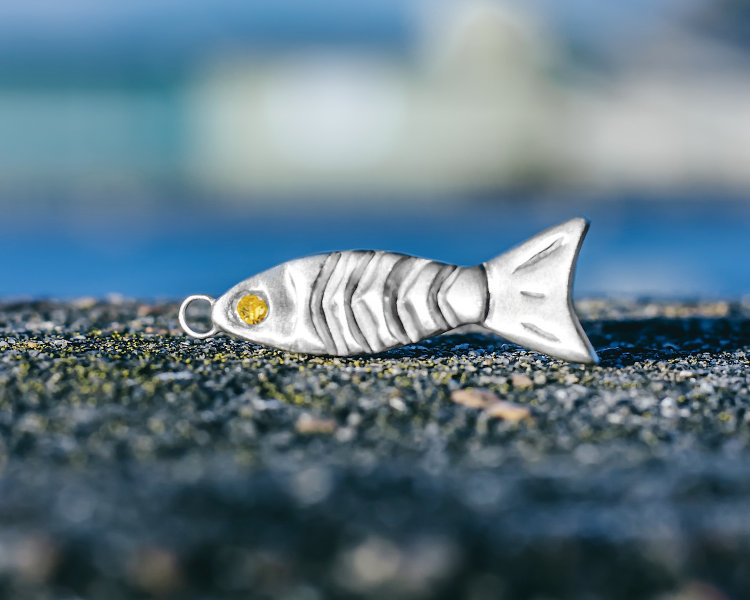 a sterling silver pendant shaped like a fish with a yellow gemstone for an eye made on a gemstone jewellery making workshop with stööki
