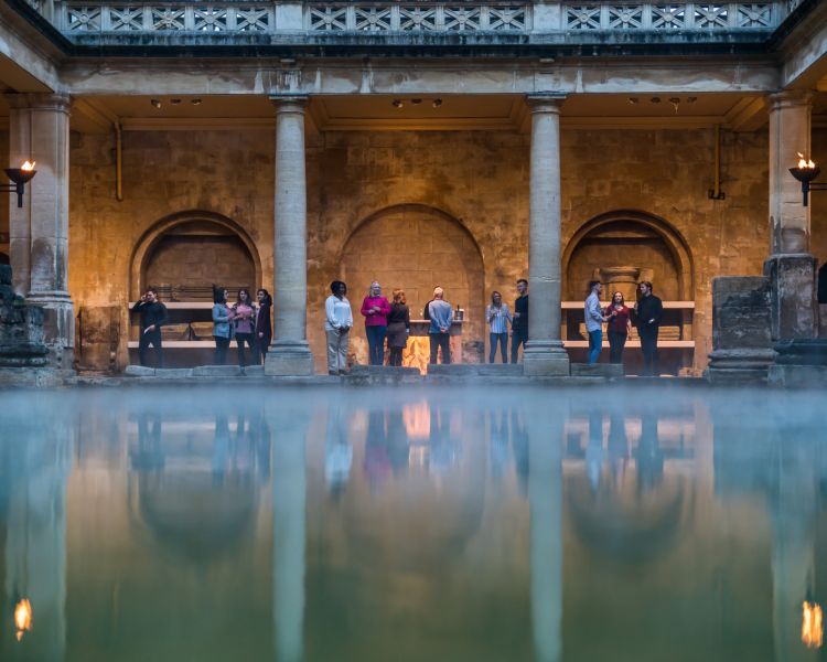 visitors in the roman baths seen across the pool with steam rising from water