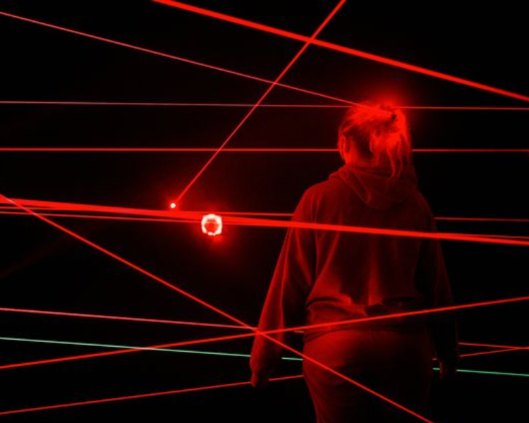 woman in dark room with red laser lights around her playing an interactive game experience