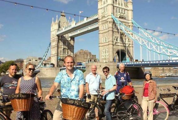 a group of people posing for a photo in front of tower bridge on a river thames bike tour