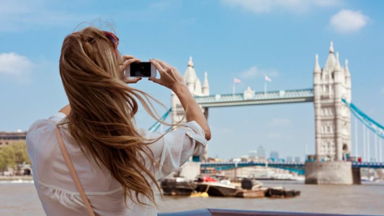 a woman taking a photo of tower bridge in London on a sightseeing visit