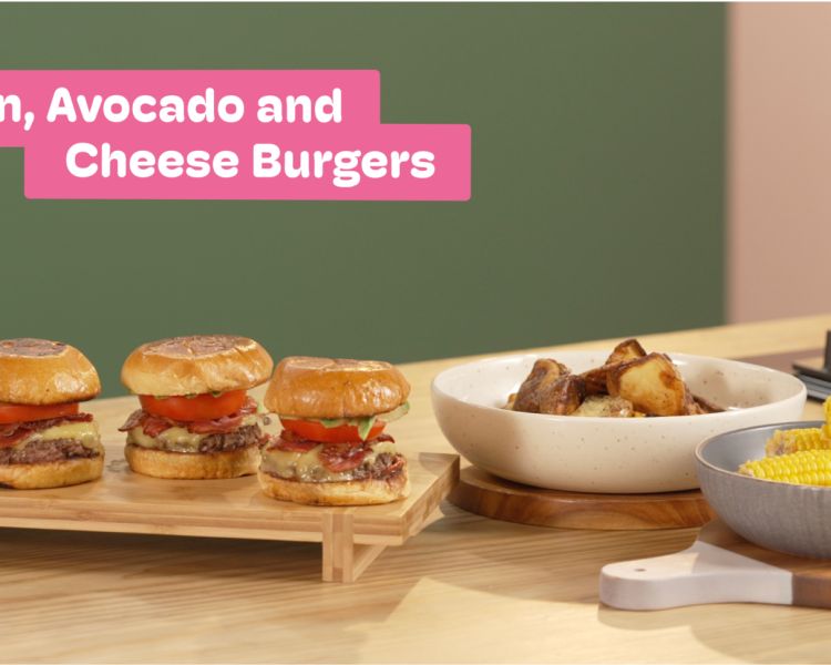 a photo showing bacon, avocado and cheese burgers next to a bowl of corn on the cob and a bowl of potatoes