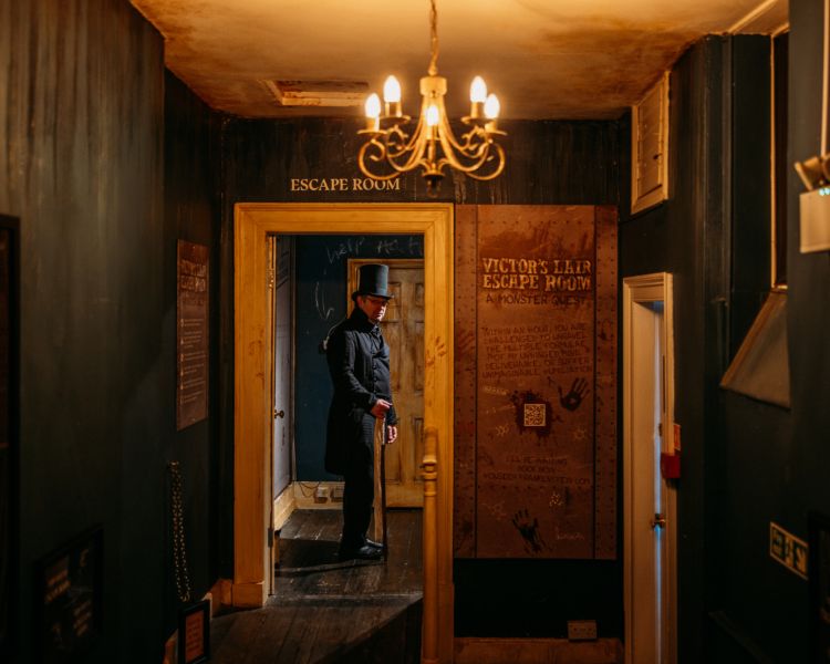 the host in character dress at the house of frankenstein showing the way to the escape room