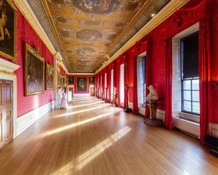 the view down a grand corridor lined with paintings on walls and a painted ceiling