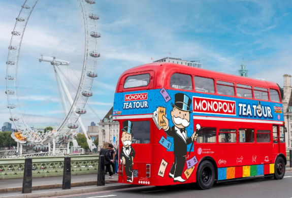 a red routemaster bus with colourful monopoly tea tour signs on it with the london eye in the background
