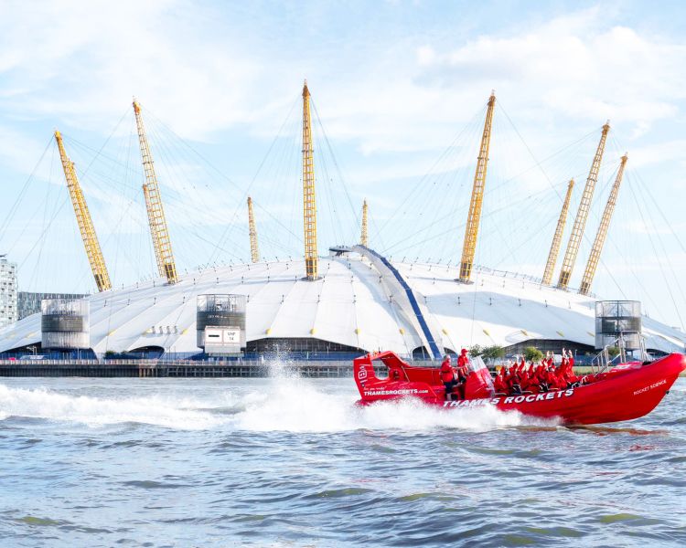a red thames rocket speedboat on the thames going past the o2 arena as part of a london speedboat experience