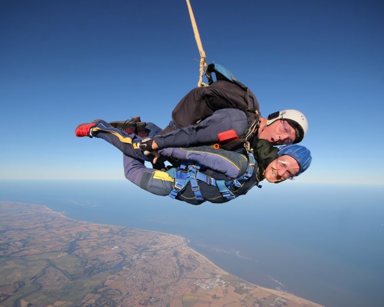 a man on a tandem skydiving experience during freefall with the coastline visible in the distance