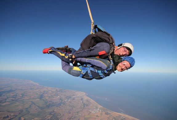 a man on a tandem skydiving experience during freefall with the coastline visible in the distance