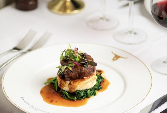 a meal of steak on top of mashed potato and greens at marco pierre white's london steakhouse company