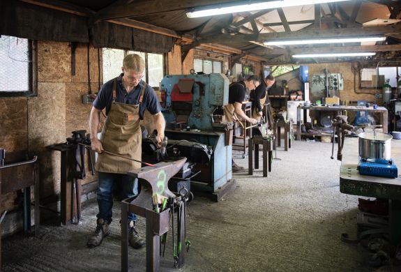 people in a forge workshop working on making a poker on a blacksmith experience