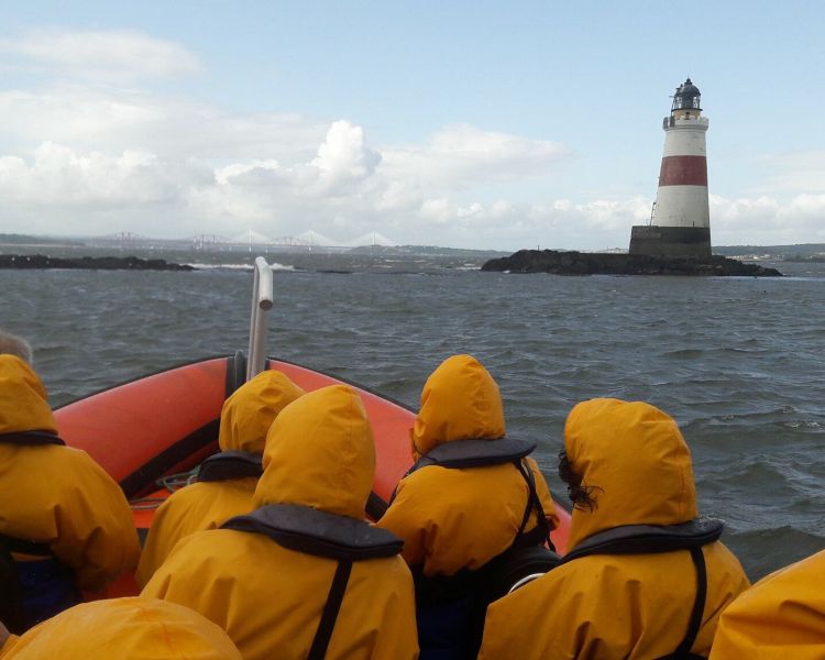 passengers wearing yellow waterproof coats looking out at a lighthouse on a high speed boat trip from south queensferry in scotland