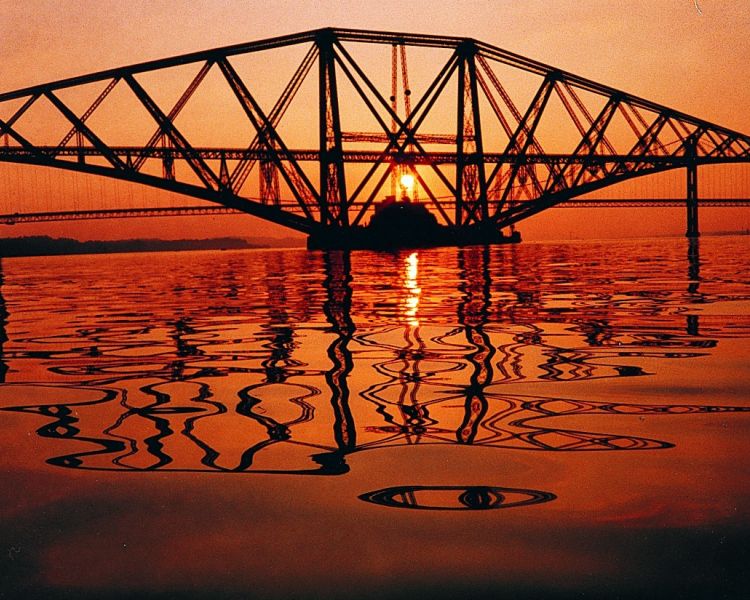 view of one of the forth bridges at sunset with the sun setting behind the bridge